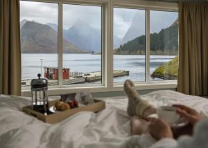 una persona sdraiata sul letto che guarda fuori da una finestra di Sagafjord Hotel - by Classic Norway Hotels a Sæbø