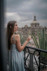 a woman standing on a balcony holding a glass of wine at Zocalo Central & Rooftop Mexico City in Mexico City