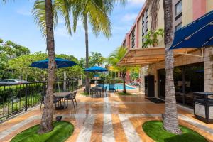 eine Terrasse mit Tischen, Stühlen und Palmen in der Unterkunft Hampton Inn Miami-Airport West in Miami