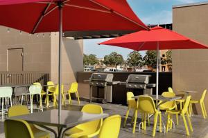 eine Terrasse mit Tischen, gelben Stühlen und roten Sonnenschirmen in der Unterkunft Home2 Suites By Hilton San Antonio North Stone Oak in San Antonio