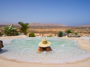 a woman in a hat sitting in a swimming pool at Alma Calma Hotel Rural in Tindaya