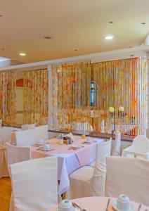 un comedor con mesas, sillas blancas y ventanas en Park Hotel, en Atenas