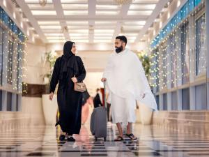 Um homem e uma mulher a andar num corredor com uma mala. em Swissotel Al Maqam Makkah em Meca