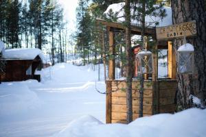 une maison extérieure en bois dans la neige à côté d'un arbre dans l'établissement Crow Creek Cabins, à Inari