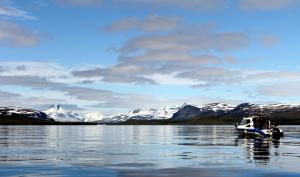 een boot in het water met besneeuwde bergen bij Saivaara Cottages in Kilpisjärvi