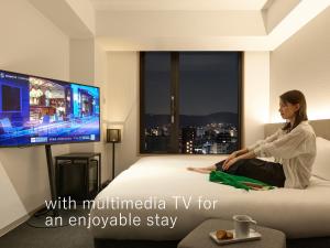 a woman sitting on a bed with multimedia tv for an enviable stay at sequence KYOTO GOJO in Kyoto