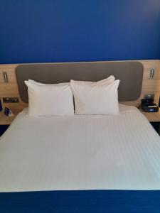 Holiday Inn Express Poole, an IHG Hotel في بول: سرير ابيض كبير ومخدات بيضاء وجدار ازرق