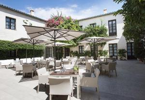 un restaurante con mesas blancas, sillas y sombrillas en Hospes Palacio del Bailio, a Member of Design Hotels, en Córdoba