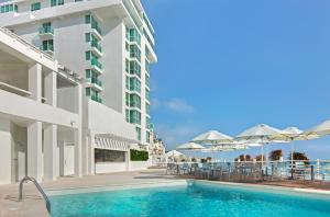 una piscina junto a un edificio con mesas y sombrillas en Oleo Cancun Playa All Inclusive Resort, en Cancún