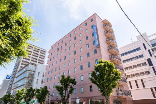 a pink building with a blue sign on it at Sanco Inn Kuwana Ekimae in Kuwana