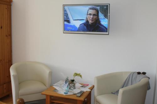 a living room with two chairs and a tv on the wall at Pension Treenehof in Friedrichstadt