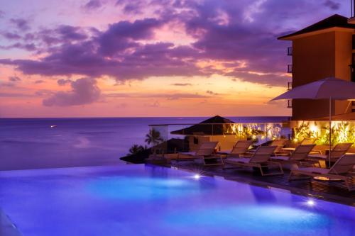 a pool with chairs and the ocean at sunset at Halepuna Waikiki by Halekulani in Honolulu