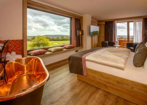 a bedroom with a tub and a bed and a window at Steig-Alm Hotel Superior in Bad Marienberg