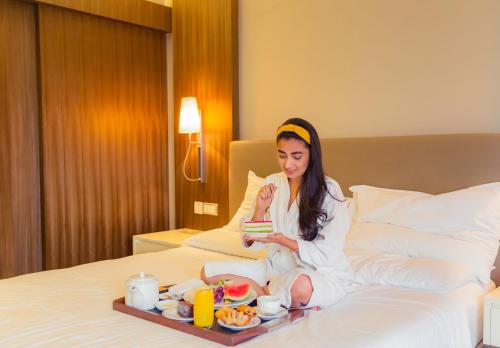 uma mulher sentada numa cama com uma bandeja de comida em Hyatt Regency Delhi em Nova Deli