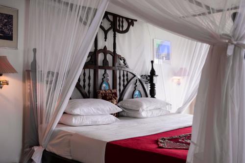 een slaapkamer met een hemelbed met witte lakens en kussens bij Tembo House Hotel in Zanzibar City