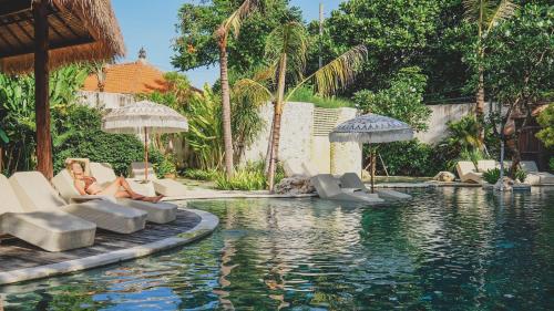 een vrouw die op stoelen naast een zwembad zit bij Amnaya Resort Nusa Dua in Nusa Dua