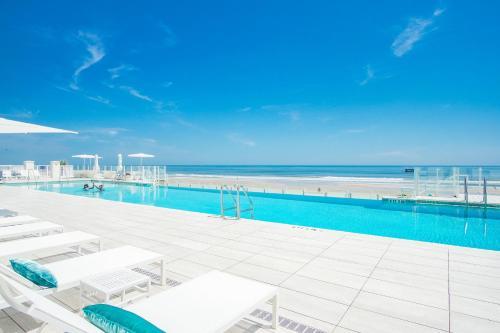 a swimming pool with white chairs and the beach at Daytona Grande Oceanfront Resort in Daytona Beach