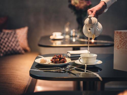 a person pouring tea from a teapot onto a plate of food at Hôtel LÉONOR the place to live in Strasbourg