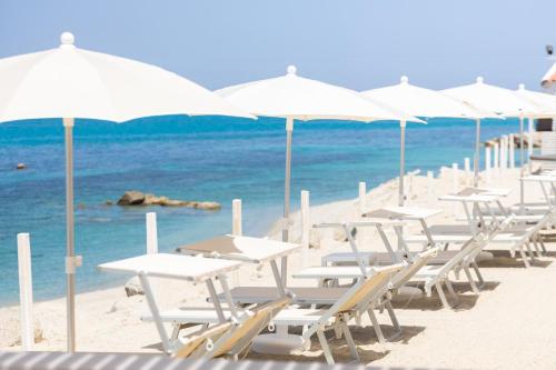 a row of white chairs and umbrellas on a beach at Midenza Seaside & Nature Retreat in Capo Vaticano