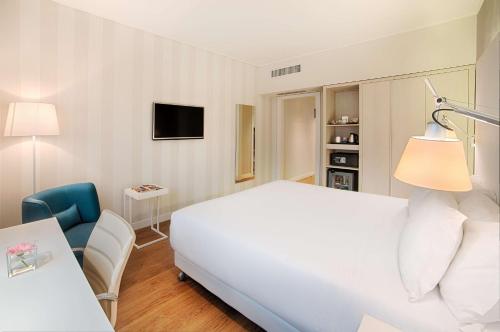 een slaapkamer met een wit bed, een tafel en een stoel bij NH Torino Centro in Turijn