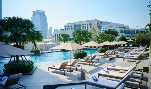 a pool with lounge chairs and umbrellas next to a city at Chatrium Grand Bangkok in Bangkok