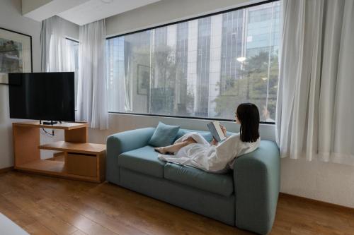 a woman sitting on a couch reading a book at Suites Coben Apartamentos Amueblados in Mexico City