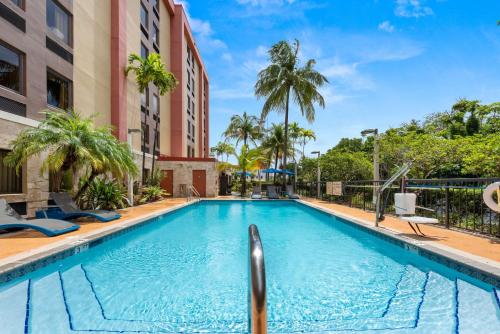 einen Pool in einem Hotel mit Palmen und einem Gebäude in der Unterkunft Hampton Inn Miami-Airport West in Miami