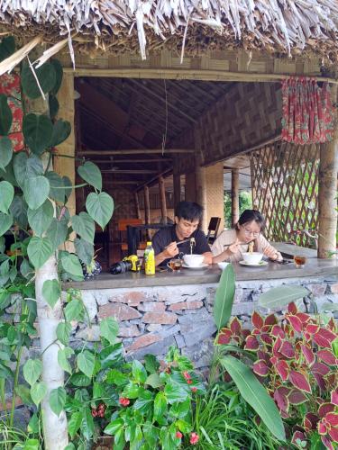 two people sitting at a table eating food at Homestay field - bungalow, Ha giang loop tour, motorbikes rental in Ha Giang