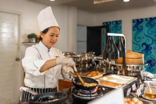 Una donna in una cucina che prepara il cibo in wok di Centara Kata Resort Phuket a Kata Beach