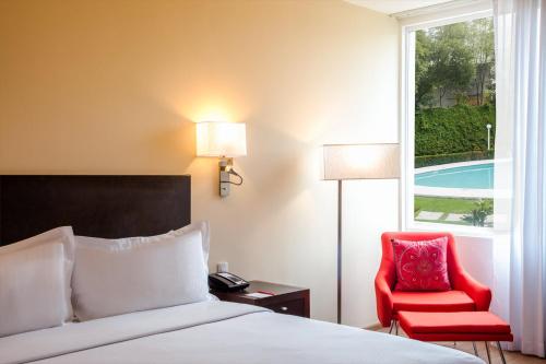 a bedroom with a bed and a red chair and a window at Fiesta Inn Aeropuerto CD Mexico in Mexico City