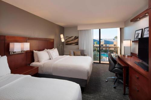 a hotel room with two beds and a desk and a television at Courtyard by Marriott Boynton Beach in Boynton Beach