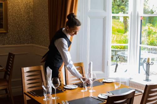 Uma mulher está a pôr uma mesa numa sala de jantar. em Killeen House Hotel em Killarney