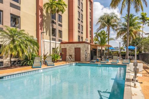 einen Pool mit Stühlen, Palmen und Gebäuden in der Unterkunft Hampton Inn Miami-Airport West in Miami