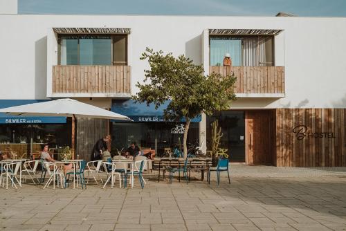 um café ao ar livre com mesas e cadeiras e um guarda-sol em B.Hostel na Comporta