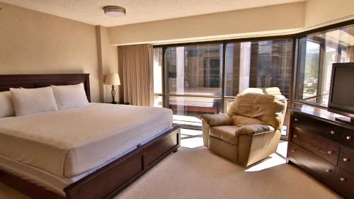 a bedroom with a bed and a chair and a television at Aston at the Executive Centre Hotel in Honolulu