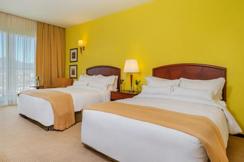 two beds in a hotel room with yellow walls at Bourbon Resort Atibaia in Atibaia