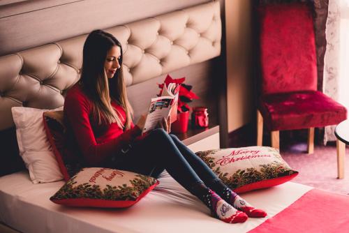 a woman sitting on a bed reading a book at Business Hotel Plovdiv in Plovdiv