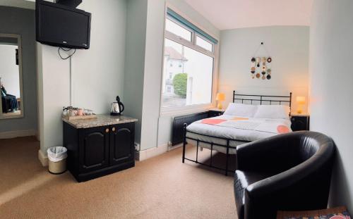 a bedroom with a bed and a chair and a television at The Sheldon B&B - FREE private parking in Eastbourne