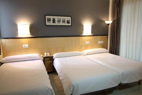 2 bedden in een hotelkamer met witte lakens bij Hotel Alda Entrearcos in Burgos