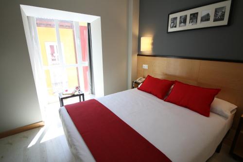 een slaapkamer met een bed met rode kussens en een raam bij Hotel Alda Entrearcos in Burgos