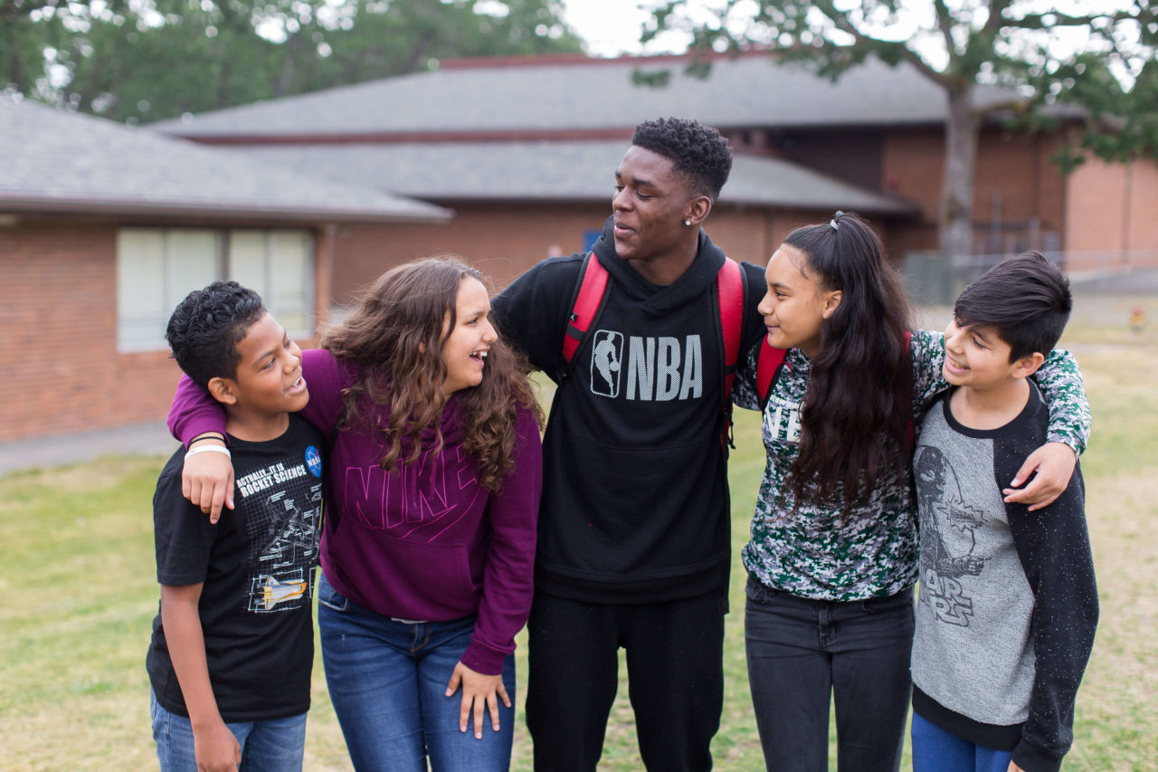 5 laughing students with arms around each other