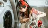 A picture of a woman wearing a red bandana putting clothes into the washing machine.