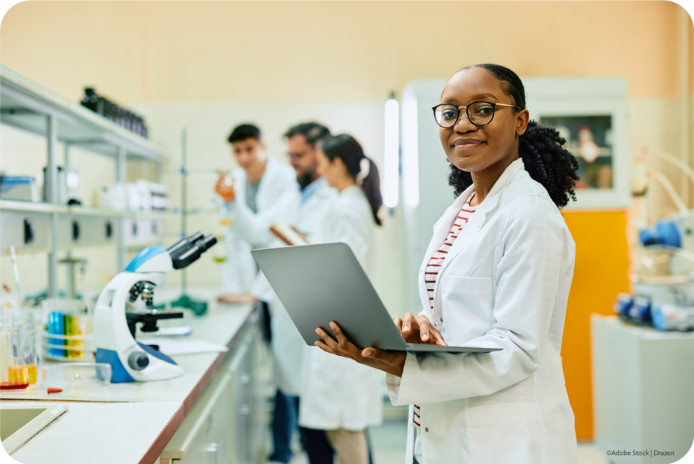 a woman scientist in the lab and a few colleagues in the background, she is holding a computer