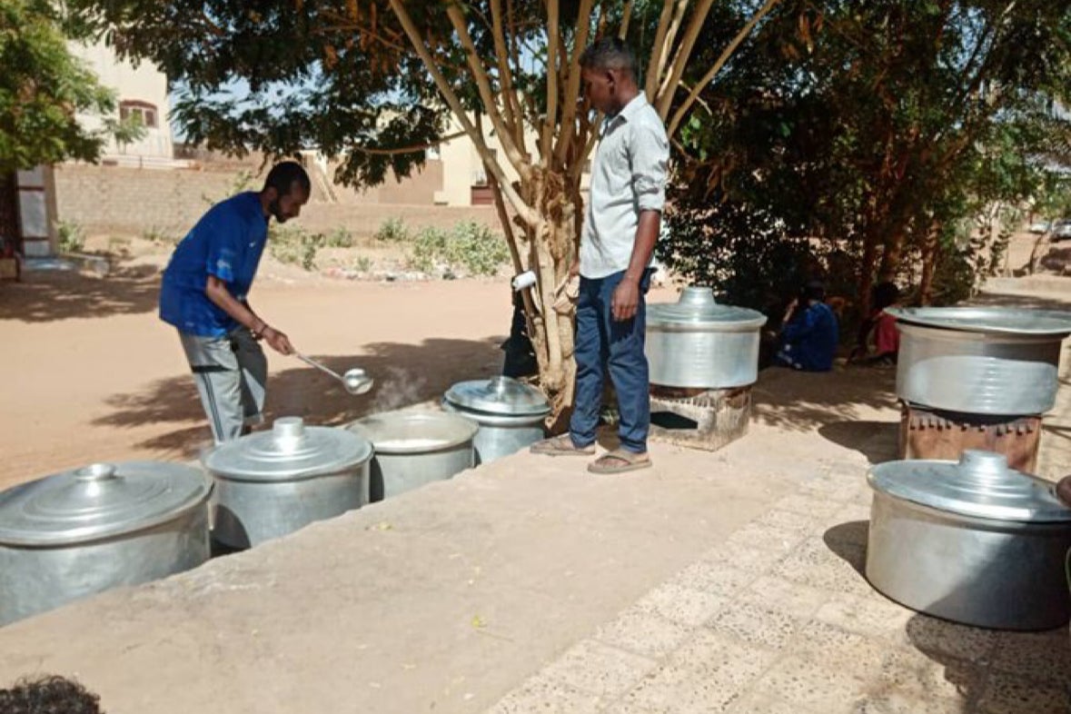 Men serve food out of huge steel pots outdoors in Sudan at a Khartoum Kitchen.