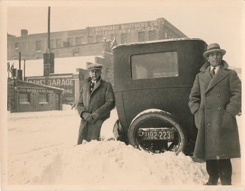 Vintage men standing next to car in snow bank.