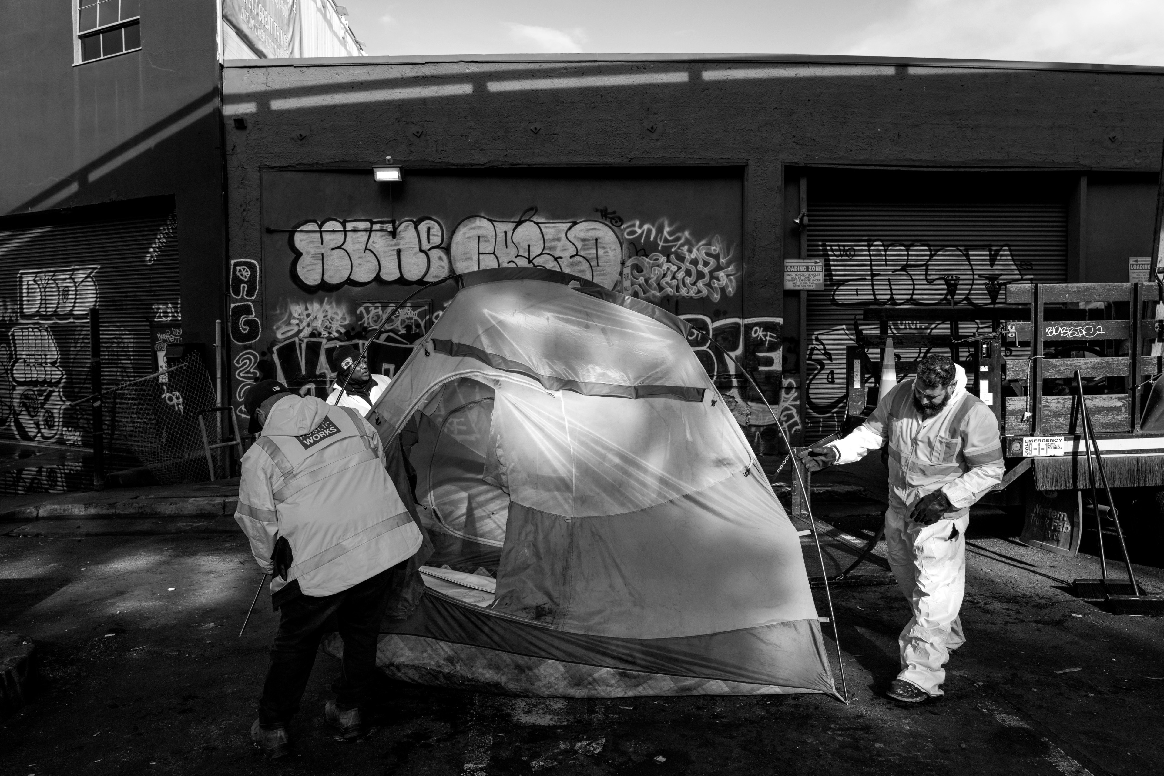 Two city workers remove a tent from a homeless encampment.