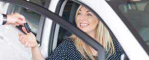 Young woman sitting in new car with key in showroom