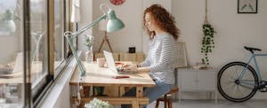 Woman sitting at a desk using a laptop computer while working from home.