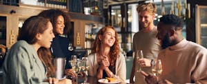 A group of friends celebrate a birthday at a restaurant and enjoy a free slice of cake.