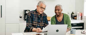 A couple seated at their kitchen island review financial documents and discuss ways to save money